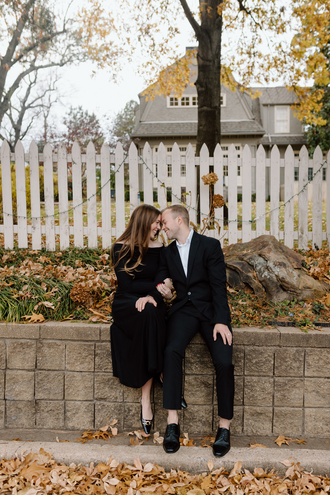 Couple sitting and laughing in front of a picket fence.